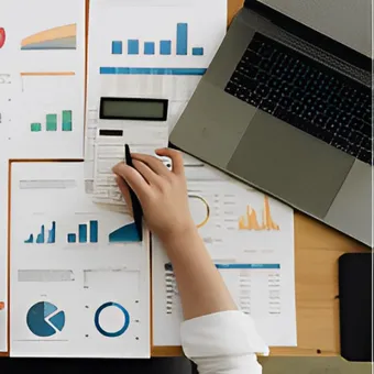 Analista che esamina grafici e report finanziari con una calcolatrice accanto a un laptop